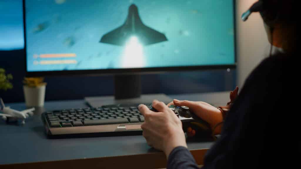 Closeup of competitive woman player holding joystick playing space shooter video games at powerful computer late night. Professional gamer using wireless controller for online gaming championship